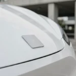 Emblème minimaliste et plat d'une marque automobile sur la calandre d'un véhicule électrique blanc, illustrant la simplification des logos de constructeurs