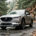 Mazda CR-V 5 en version argent garé sur une route de montagne sinueuse entouré de sapins