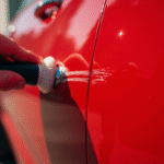 Main polissant une rayure sur une porte de voiture rouge brillante